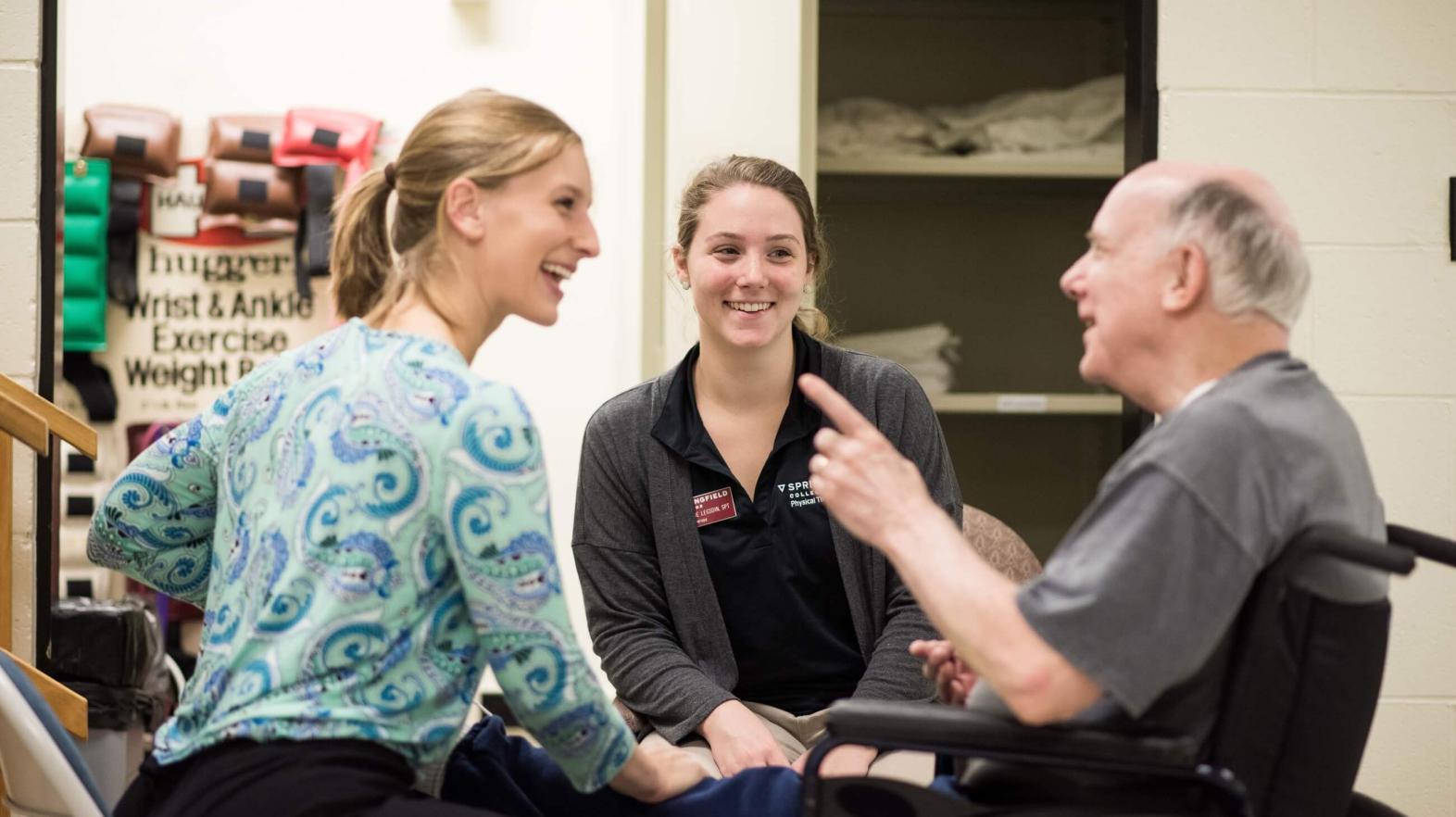 Physical therapy students talk with a patient in a wheelchair. 
