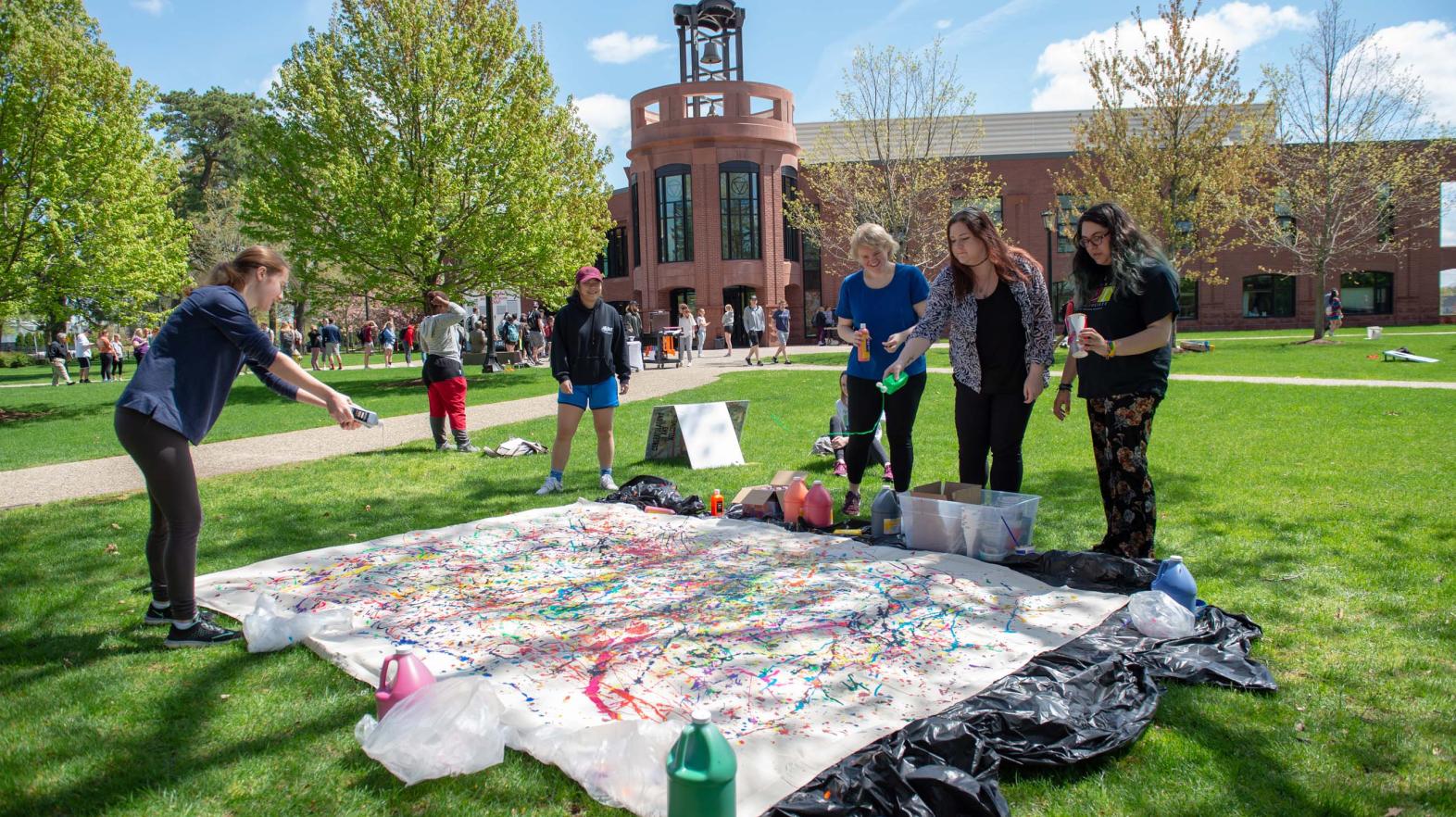Students throw paint on a tarp on the quad. 
