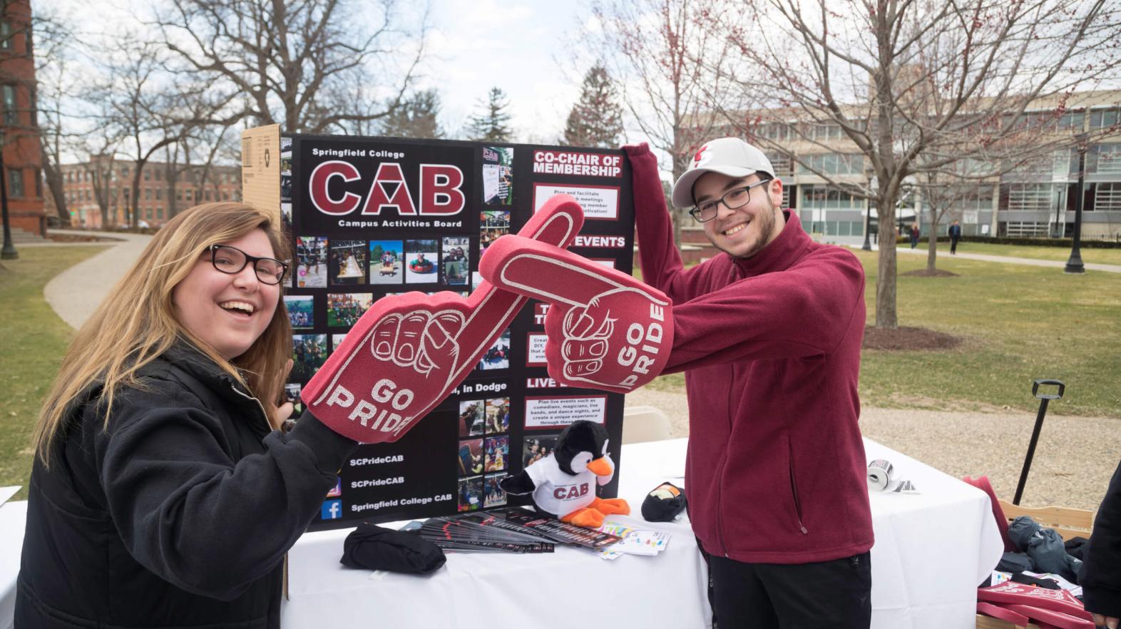 Two students stand with foam fingers in front of information about their club.