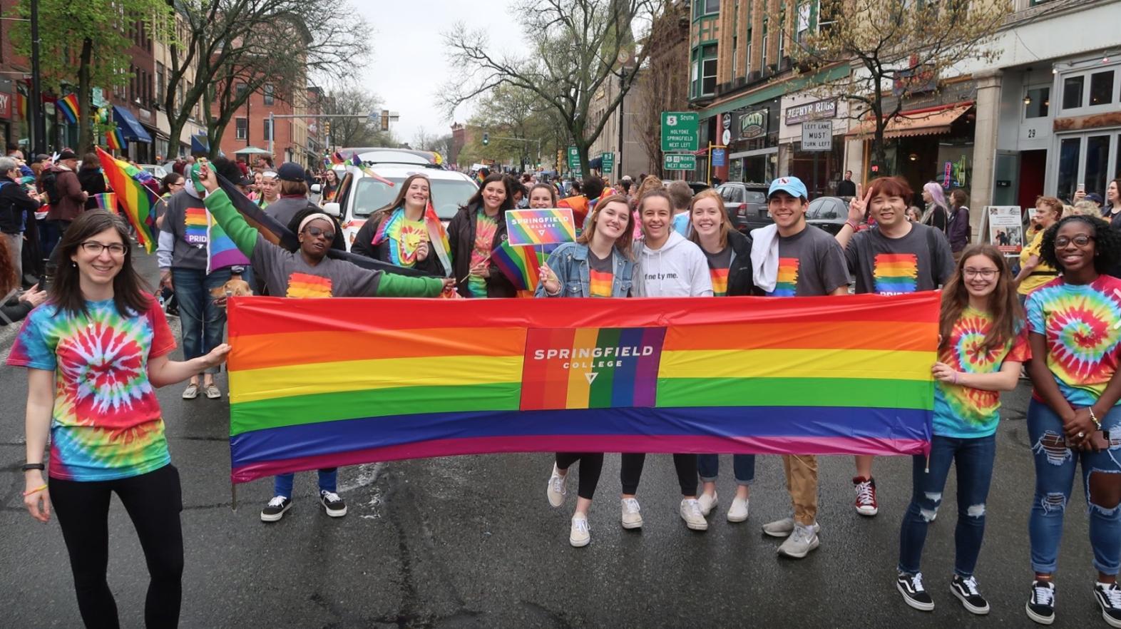 Students march with a rainbow Springfield College sign at a Pride Parade. 