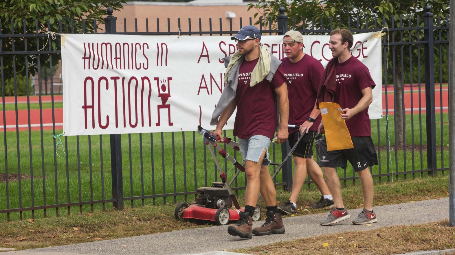 Students carry yard work supplies past a Humanics in Action day sign. 