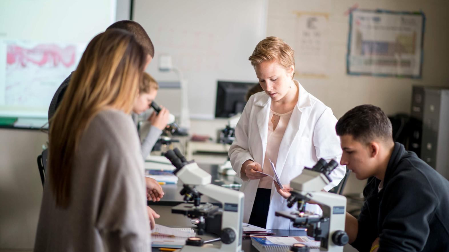 A professor works with her students and microscopes. 