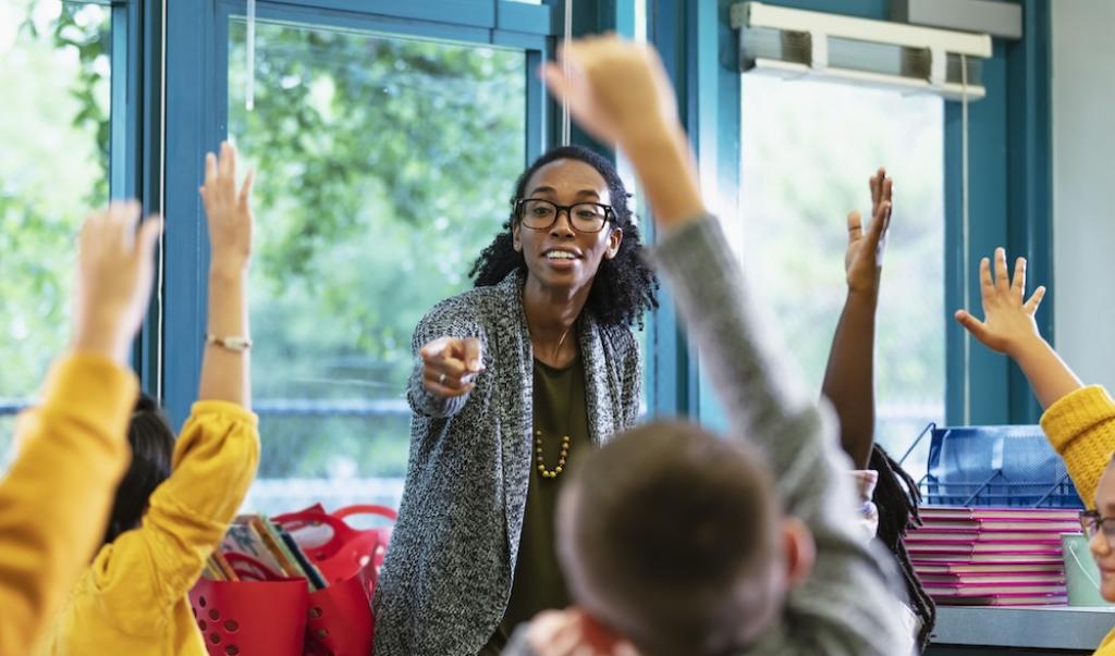 Teacher in classroom points to student raising hand stock photo