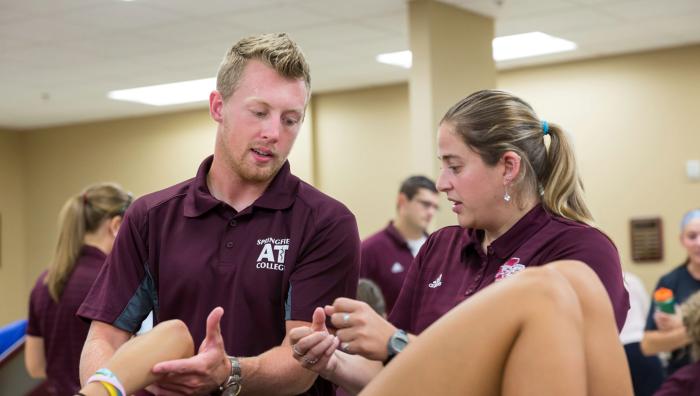 Two athletic training students working on a client's arm in an athletic training facility.