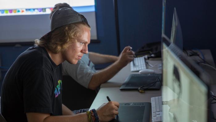Student sitting infront of computer working on graphics project.