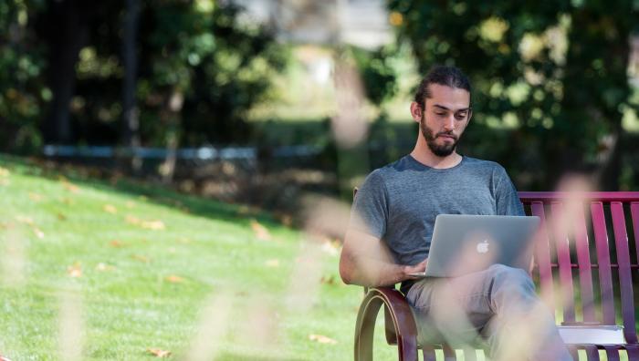 Student sitting on bench outside using a laptop