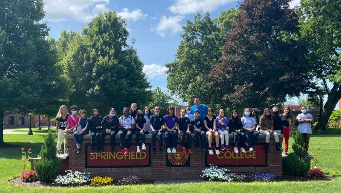 7th grade students visiting campus sitting on Springfield College sign
