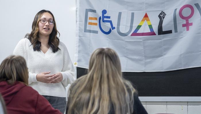 teacher in class standing in front of a sign that says equality